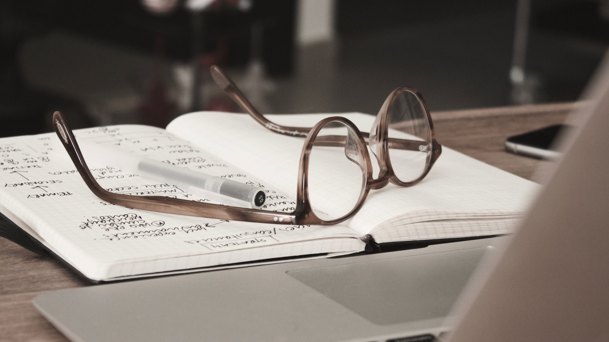 Brown glasses sitting on a research notebook by a laptop.