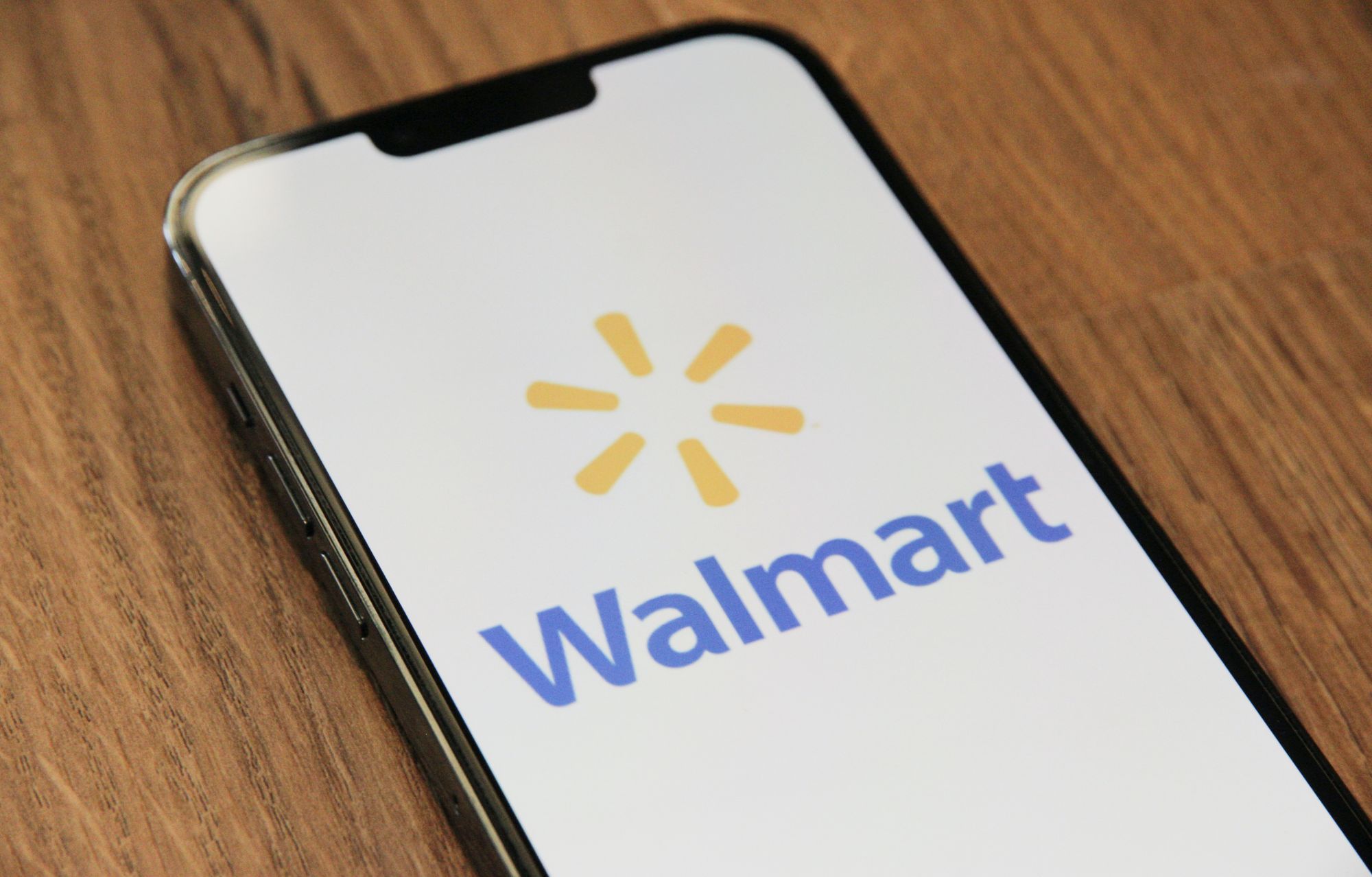 The Walmart logo on a phone screen, sitting on a wooden background.