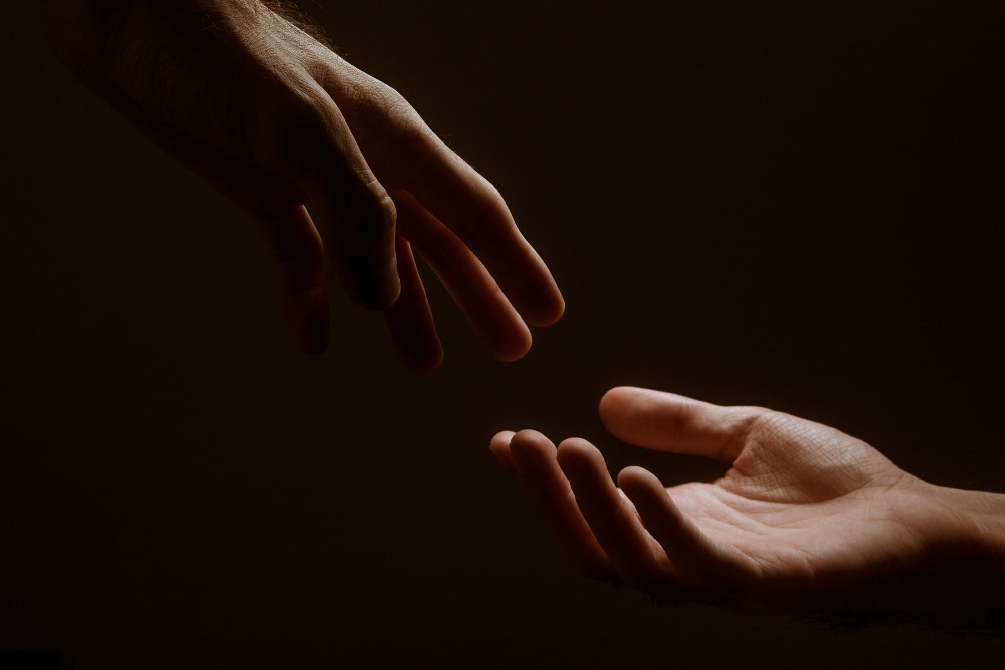 Two hands reaching for each other in darkness.