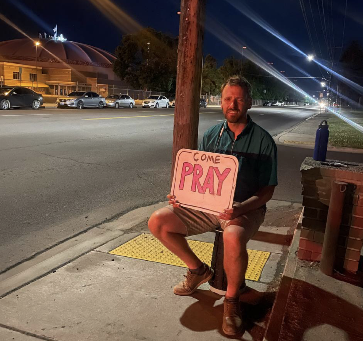Man holds sign saying "Come Pray."