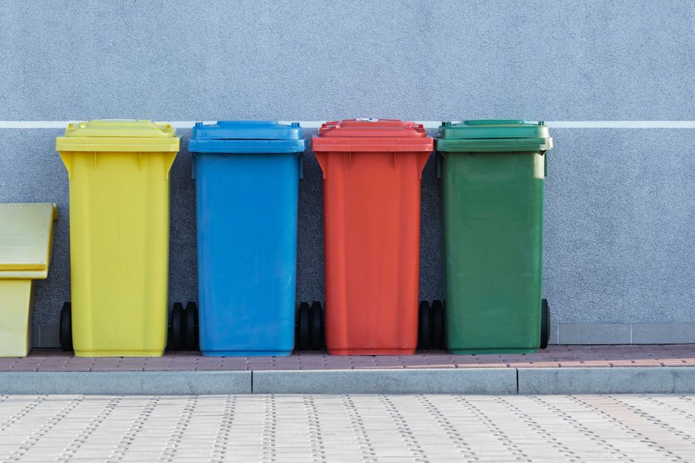 Four assorted color garbage cans on a curb awaiting pickup.