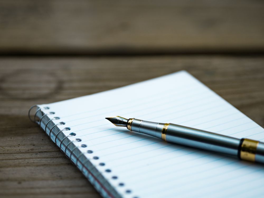 Calligraphy pen sitting on a notebook on a wooden table.