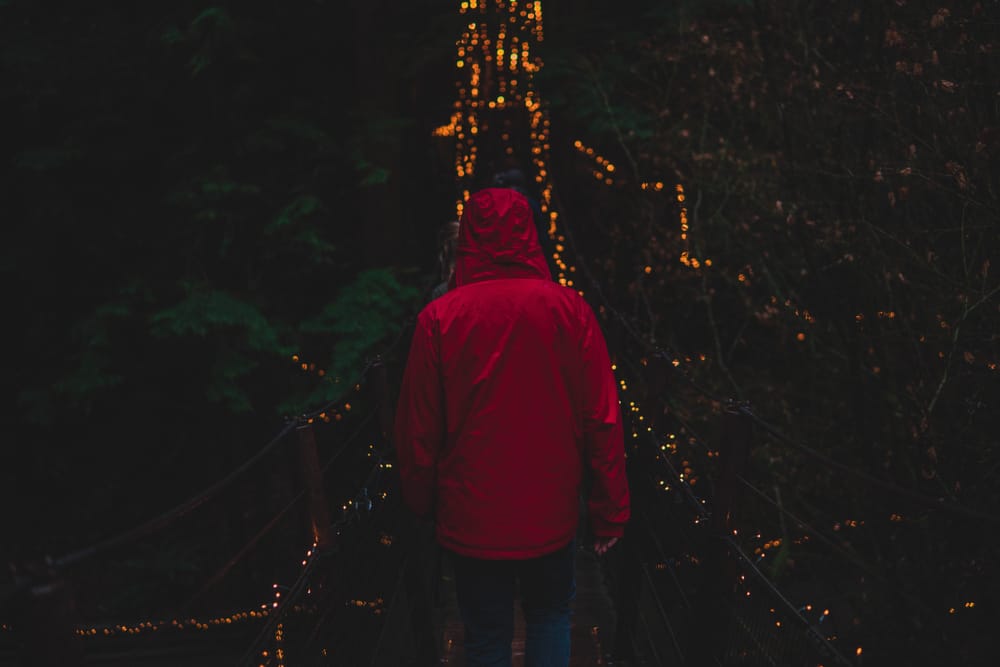 Man in red jacket crosses bridge with lights.